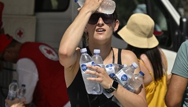 امرأة تبرّد جبهتها بزجاجة ماء بارد وزعتها منظمة الصليب الأحمر اليونانية بالقرب من مدخل موقع أكروبوليس الأثري في أثينا (20 تموز 2023، أ ف ب).