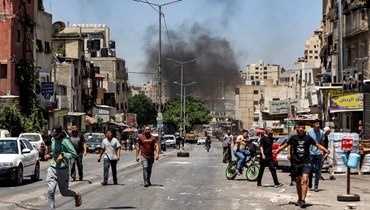أشخاص يمشون في شارع بينما تصاعد دخان من إطارات محترقة على طريق خلال اقتحام الجيش الإسرائيلي مخيم العين للاجئين الفلسطينيين غرب نابلس بالضفة الغربية المحتلة (26 تموز 2023، أ ف ب). 