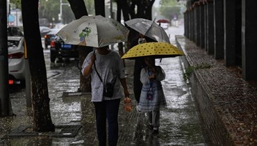 اشخاص يمشون تحت مظلات خلال هطول الامطار في بيجينغ (30 تموز 2023، أ ف ب). 