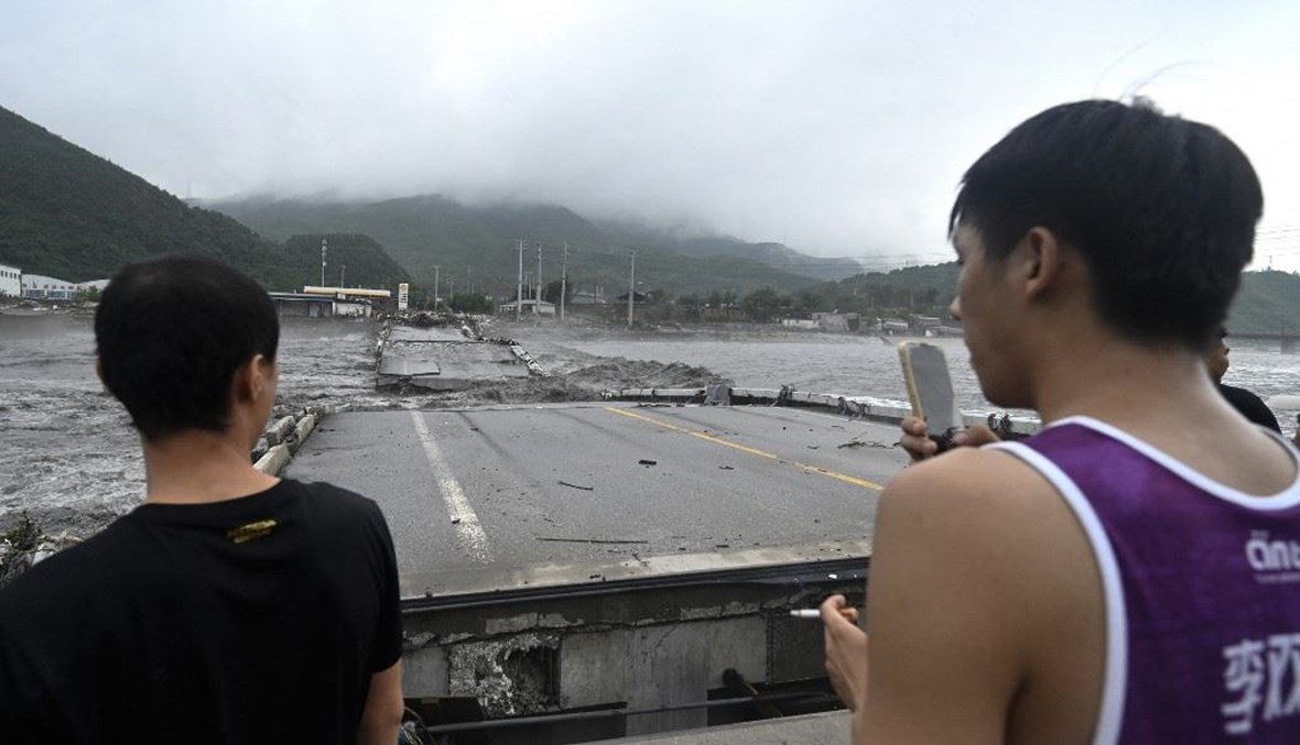 أشخاص ينظرون الى جسر منهار فوق نهر داشيخه بعد هطول أمطار غزيرة في منطقة فانغشان في بيجينغ (1 آب 2023، أ ف ب).