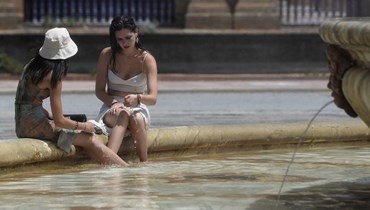 فتاتان غطستا أقدامهما في ماء نافورة في ساحة بلازا دي إسبانيا في إشبيلية (7 آب 2023، أ ف ب).