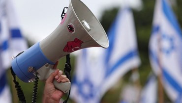 متظاهر يستخدم مكبّر الصوت ليردّد الشعارات خلال مسيرة ضدّ خطة الإصلاح القضائي للحكومة الإسرائيلية في تل أبيب (أ ف ب). 