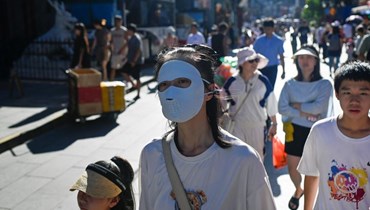 امرأة وضعت قناعا على الوجه خلال سيرها في أحد الشوارع التجارية في بيجينغ (22 آب 2023، أ ف ب). 