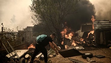 أحد السكان المحليين يزيل قطعا من الخشب مع انتشار حريق غابات بالقرب من منزل في أتشارنيس شمال أثينا (23 آب 2023، أ ف ب).