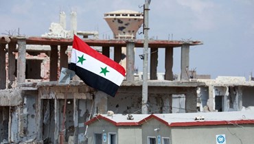 علم سوري فوق أبنية متضرّرة في منطقة درعا البلد التابعة لمدينة درعا جنوب سوريا (تعبيرية- أ ف ب).