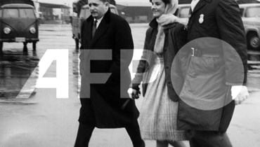 شرطي يرافق بريسيلا بوليو الزوجة السابقة لنجم الروك الأميركي الراحل إلفيس بريسلي في القاعدة الجوية العسكرية في فرانكفورت في 2 آذار 1960 (أ ف ب). 