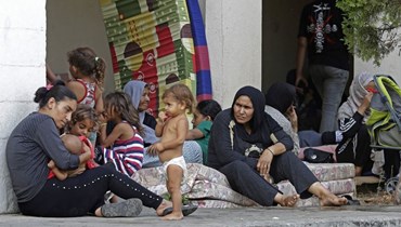 نساء يجلسن مع أطفالهن بعد فرارهن من مخيّم عين الحلوة (أ ف ب)