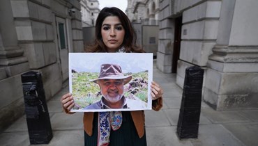 صورة ارشيفية- روكسان طهباز تحمل صورة والدها مراد طهباز المسجون في إيران، خلال احتجاج خارج مقر وزارة الخارجية البريطانية في لندن (13 نيسان 2022، أ ب). 