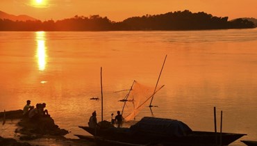 رجل يلقي شبكة صيد في نهر مع غروب الشمس في جواهاتي (أ ف ب). 