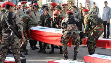جنود سوريون يحملون توابيت خلال جنازة ضحايا هجوم بطائرة بدون طيار استهدف أكاديمية عسكرية سورية (أ ف ب).