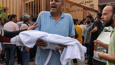 رجل يحمل جثة طفل فلسطيني قُتل في غارة جوية إسرائيلية لدفنها في خان يونس بجنوب قطاع غزة (11 ت1 2023، أ ف ب).