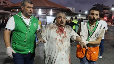رجال الطوارئ يساعدون رجلا فلسطينيا مصابا في مستشفى الشفاء في مدينة غزة بعد غارة جوية إسرائيلية (11 ت1 2023، أ ف ب). 