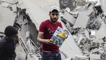 رجل حمل غلاف مجلة عليه صورة لمسجد قبة الصخرة بينما وقف أمام مبنى متضرر من جراء غارة إسرائيلية على رفح في جنوب قطاع غزة (15 ت1 2023، أ ف ب).