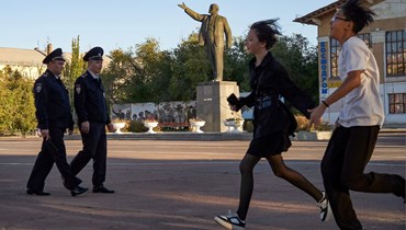 شباب يركضون في ساحة في بايكونور بينما يقوم شرطيون بدوريات فيها (16 ت1 2023ـ أ ف ب).