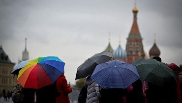 سياح يحتمون من المطر تحت مظلات خلال زيارتهم الساحة الحمراء وسط موسكو (18 ت1 2023، أ ف ب). 