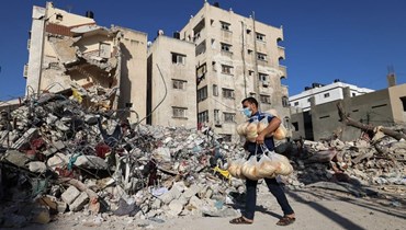 عامل فلسطيني يمر بالقرب من أنقاض مبنى دمرته الغارات الاسرائيلية في مدينة غزة (27 ايار 2021، أ ف ب).