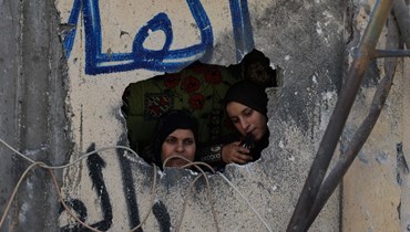 نساء فلسطينيات ينظرن من فتحة في جدار متضرر بعد الغارات الإسرائيلية على مخيم رفح للاجئين في جنوب قطاع غزة (25 ت1 2023، أ ف ب).