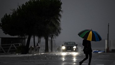 امرأة تحمل مظلة بينما تعبر شارعا تحت المطر في أركاشون جنوب غرب فرنسا قبل العاصفة سياران (1 ت2 2023، أ ف ب).