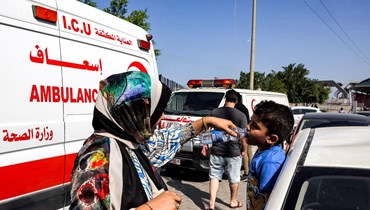 امرأة تساعد طفلاً على شرب الماء أثناء انتظاره بجوار سيارات الإسعاف التابعة لوزارة الصحة الفلسطينية في انتظار دخول معبر رفح الحدودي مع مصر (أ ف ب). 