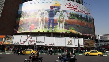 أشخاص يسيرون أمام لوحة إعلانية كبيرة  في طهران، تجسّد قتل الأطفال في غزة (أ ف ب). 