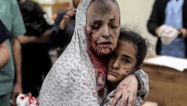 أم تحضن ابنتها في مستشفى دير البلح بعد إصابتهما بالقصف الإسرائيلي في غزة (أ ف ب).