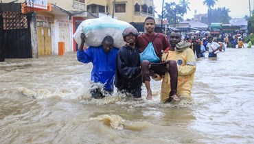 أشخاص يحاولون عبور شارع غمرته المياه بعد هطول أمطار غزيرة في منطقة كيمبيني في مومباسا (17 ت2 2023، أ ف ب). 