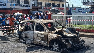 أشخاص ينظرون إلى سيارة محترقة في مونروفيا، صدمت حشدا من أنصار الحزب المتحد خلال احتفالهم بفوز بواكاي (21 ت2 2023، أ ف ب).