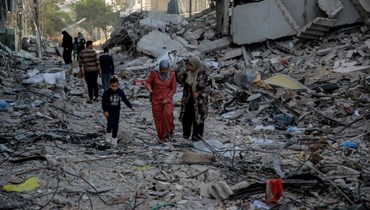 فلسطينيون يمشون بين ابنية مدمرة في مدينة غزة (26 ت2 2023، أ ف ب). 