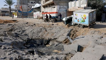 فلسطينيّون  أمام حفرة عقب غارة جوية إسرائيليّة على الطريق الرئيسي بين رفح وخان يونس في جنوب قطاع غزة (أ ف ب). 