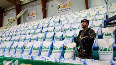 رجل أمن يمني وقف بجوار إمدادات غذائية التي قدمتها هيئة الزكاة الخيرية التي يديرها الحوثيون لتوزيعها على المحتاجين في صنعاء (4 ك1 2023، أ ف ب). 
