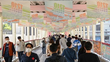 أشخاص يعبرون تحت ملصقات انتخابية تروج لانتخابات مجالس المقاطعات المقبلة في هونغ كونغ (8 ك1 2023، أ ف ب).