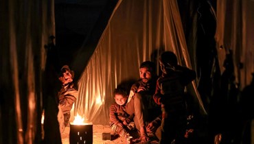 رجل وأطفال يجلسون حول النار خارج إحدى خيم النزوح جرّاء الحرب على غزة (أ ف ب). 