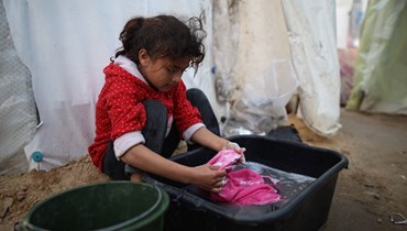 فتاة فلسطينيّة نازحة تغسل ملابسها في حوض، في محيط مستشفى في دير البلح وسط قطاع غزة (أ ف ب). 
