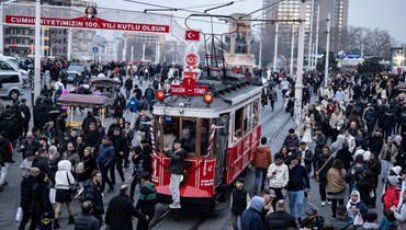 أشخاص يمرون بجوار ترام تاريخي في ميدان تقسيم خلال الاستعدادات للاحتفال بالسنة الجديدة 2024 في إسطنبول (31 ك1 2023، أ ف ب). 