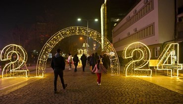 اشخاص يمشون قرب زينة معروضة في وسط  بريشتينا بمناسبة رأس السنة الجديدة (30 ك1 2023ـ أ ف ب). 