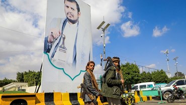 مقاتلون يمنيون يمرون قرب صورة كبيرة للزعيم الحوثي عبد الملك الحوثي في أحد شوارع صنعاء (18 ك2 2024، أ ف ب). 