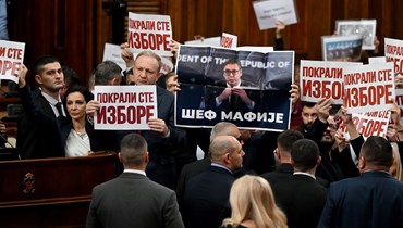 نواب معارضون يحملون لافتات كتب عليها "لقد سرقتم الانتخابات" وملصقًا للرئيس الصربي ألكسندر فوتشيتش مع نص "زعيم المافيا"، خلال الجلسة الأولى للجمعية الوطنية الجديدة في بلغراد (6 شباط 2024، أ ف ب). 