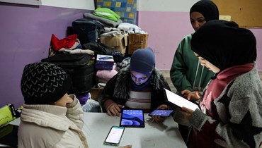 طلاب نازحون في إحدى مراكز الإيواء في مدارس صور يتابعون دروسهم عبر الأجهزة الالكترونية (أف  ب).