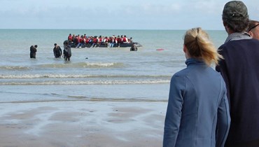 أشخاص على شاطئ سانغات شمال فرنسا يراقبون مهاجرين في قارب مطاطي قبل محاولتهم عبور القنال الإنكليزي بشكل غير قانوني للوصول إلى بريطانيا (18 تموز 2023، أ ف ب).