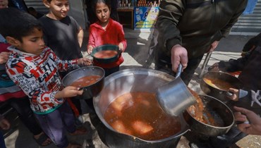 أطفال فلسطينيون يحصلون على حصص غذائية مطبوخة كجزء من مبادرة شبابية تطوعية في رفح بجنوب قطاع غزة (5 آذار، 2024 - أ ف ب).