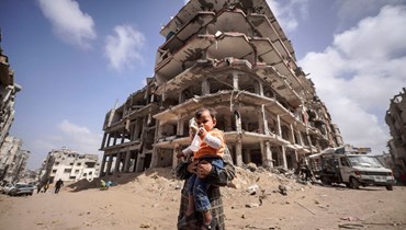 امرأة فلسطينية وطفلها يقفان أمام أنقاض مبنى دمّره القصف الإسرائيلي في خان يونس، جنوب قطاع غزة (6 آذار 2024 - أ ف ب).