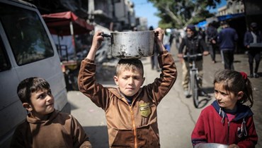 أطفال يحملون أدوات المطبخ وهم يسيرون نحو نقطة توزيع المواد الغذائية في خان يونس بجنوب قطاع غزة في "7 آذار 2024 - أ ف ب".