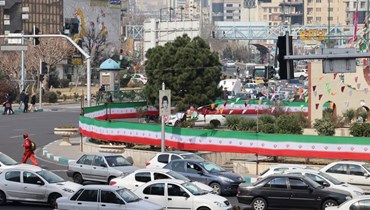 سيارات تمر بجوار جدار مغطى بلافتة بألوان العلم الوطني في طهران (3 آذار 2024 - أ ف ب).