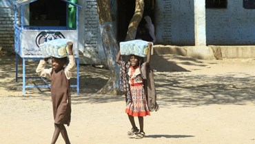 أطفال سودانيون نازحون يحملون مساعدات إنسانية في مدرسة  لجأت إليها أسرهم، بالقرب من مدينة القضارف في السودان (6 آذار 2024، أ ف ب).