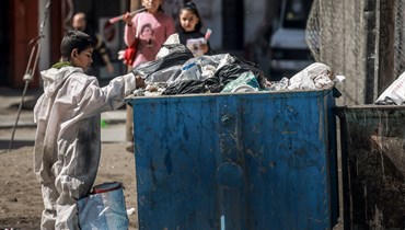 فتى فلسطيني يبحث في القمامة عن كرتون لإشعال النار، في مخيم رفح جنوب قطاع غزة (21 آذار 2024 - أ ف ب).