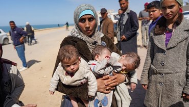 سيدة فلسطينية تحمل أطفالها بعد إخلاء مستشفى الشفاء (أ ف ب).