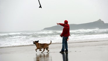رجل يرمي عصا لكلبه على شاطئ غراند بلاج في  فرنسا (أ ف ب). 
