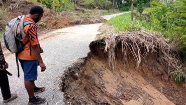 مواطنون يقفون على الطريق الذي تضرّر بسبب الانهيار الأرضي في بابوا غينيا الجديدة (أ ف ب). 