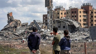 شباب يراقبون من بعيد بينما يقوم الناس بتفتيش أنقاض المباني المدمرة في مجمع أسرا السكني، شمال غرب النصيرات في قطاع غزة (25 آذار، 2024 - أ ف ب).
