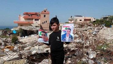 فتى يرفع صورة شهيد في الناقورة على أنقاض مبنى مدمّر جرّاء الغارات الإسرائيلية الأخيرة ليل الأربعاء (أحمد منتش).
